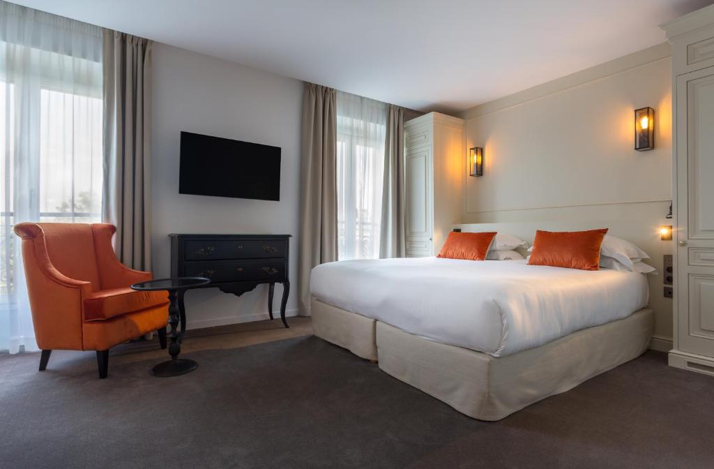Hôtel La Comtesse room with a large bed, orange pillows, and soft lighting. An orange armchair and small table are near the window with curtains.