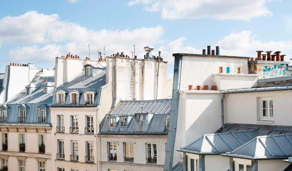 A rooftop view of Parisian buildings, showcasing classic architecture, chimneys, and a clear blue sky.