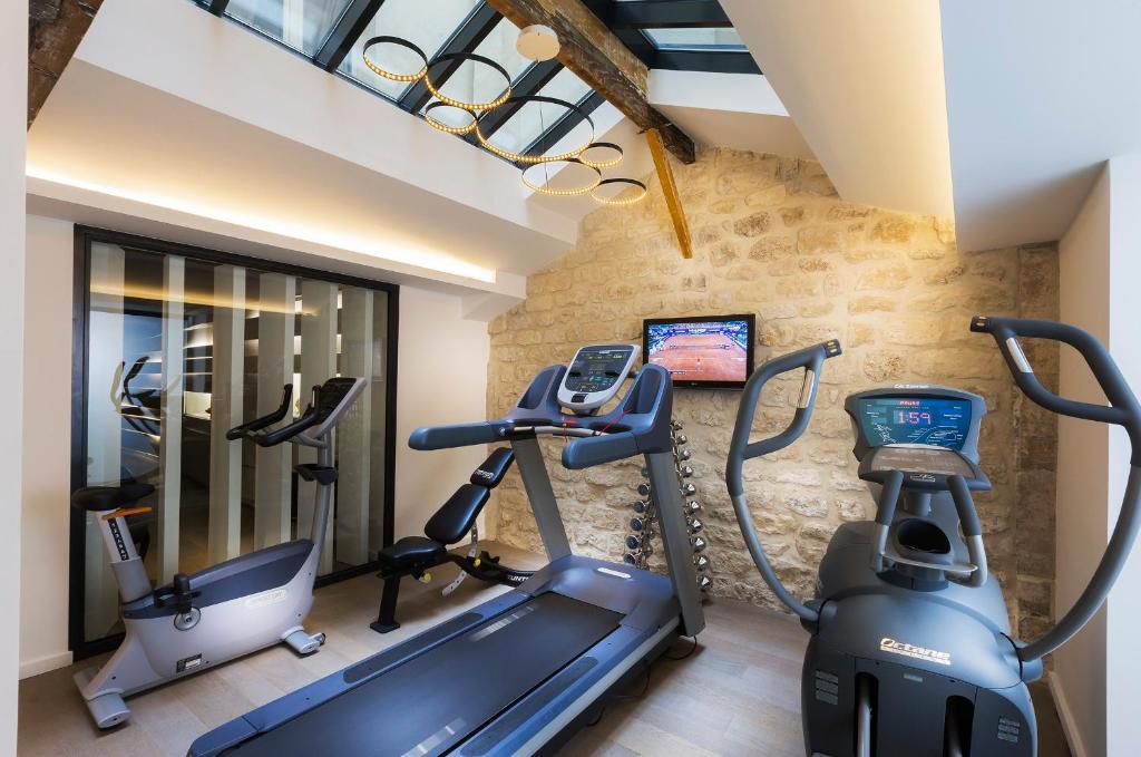 A compact hotel gym with modern exercise equipment under a skylight, set against exposed stone walls for a unique workout experience.