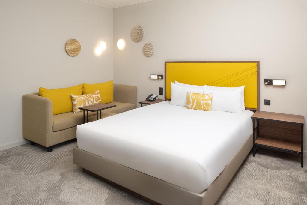 Interior of a hotel room with a bed, couch, and yellow accents at Hyatt Place Paris Charles de Gaulle Airport.