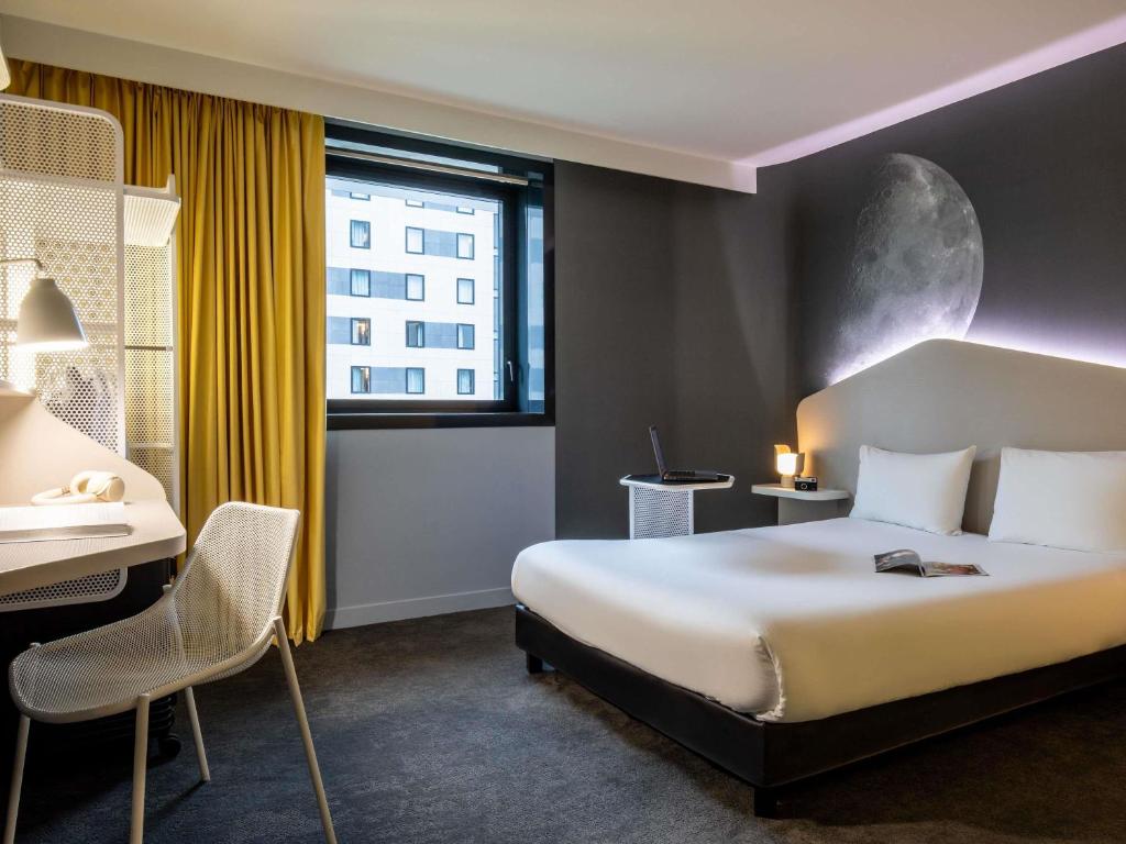Hotel room at ibis Styles Paris CDG Airport featuring a bed, desk, and large window with natural light.