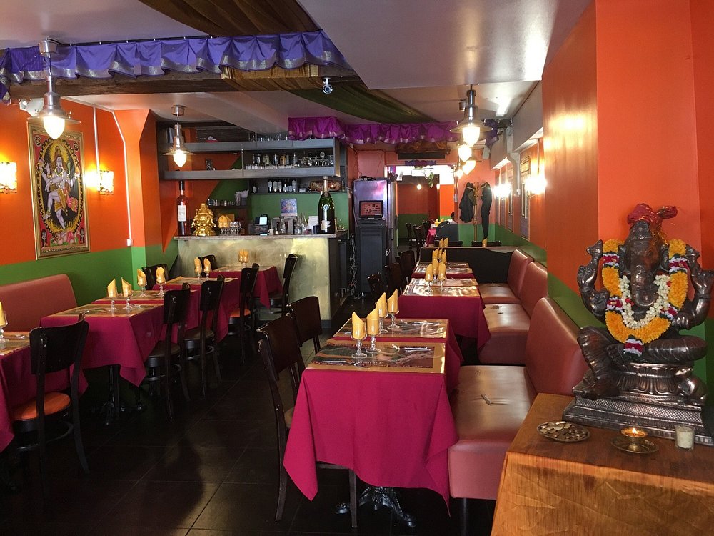 Krishna Bhavan cozy Indian restaurant interior with vibrant orange and green walls, purple drapes, and red tablecloths. Tables are set with napkins. Ganesh statue adds char in Paris