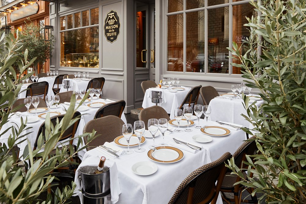 Outdoor seating area at La Maison de la Truffe restaurant in Paris, featuring tables and chairs under a clear sky