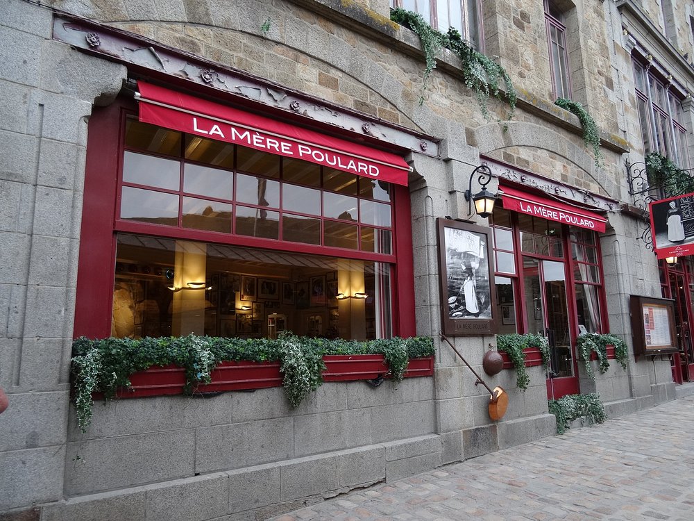 Brick structure featuring red windows and a sign that says "La Mère Poulard" located in La Mère Poulard, France.