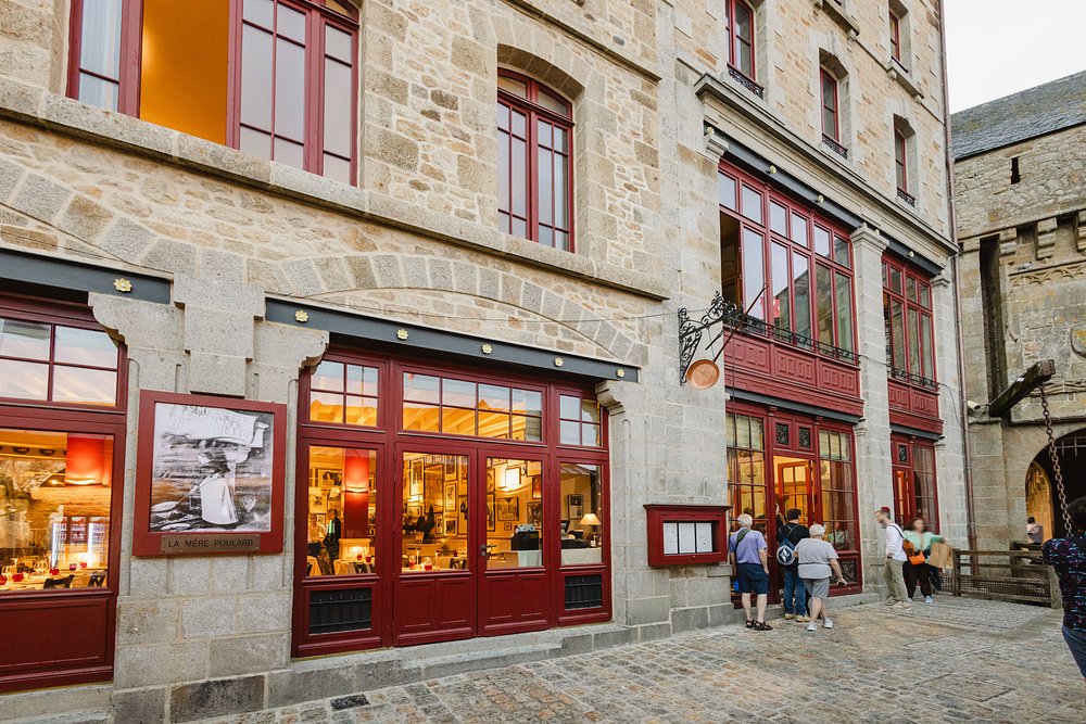 People walking in front of La Mère Poulard restaurant in a bustling city in France.