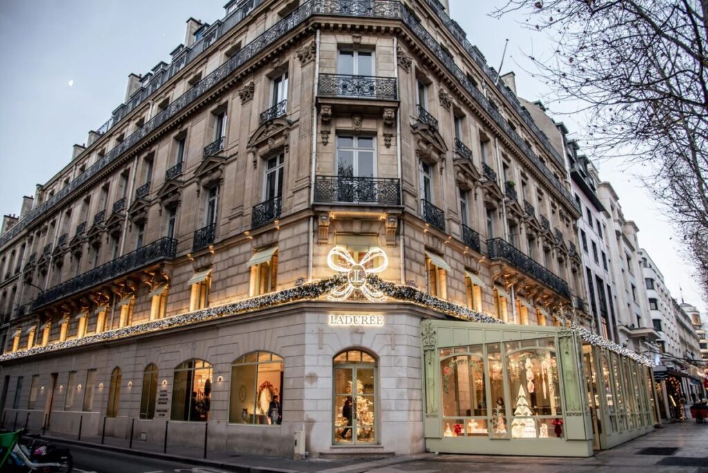 Elegant corner building adorned with festive lights, featuring "Laduree" signage. A glow emanates from the windows, conveying warmth and charm.