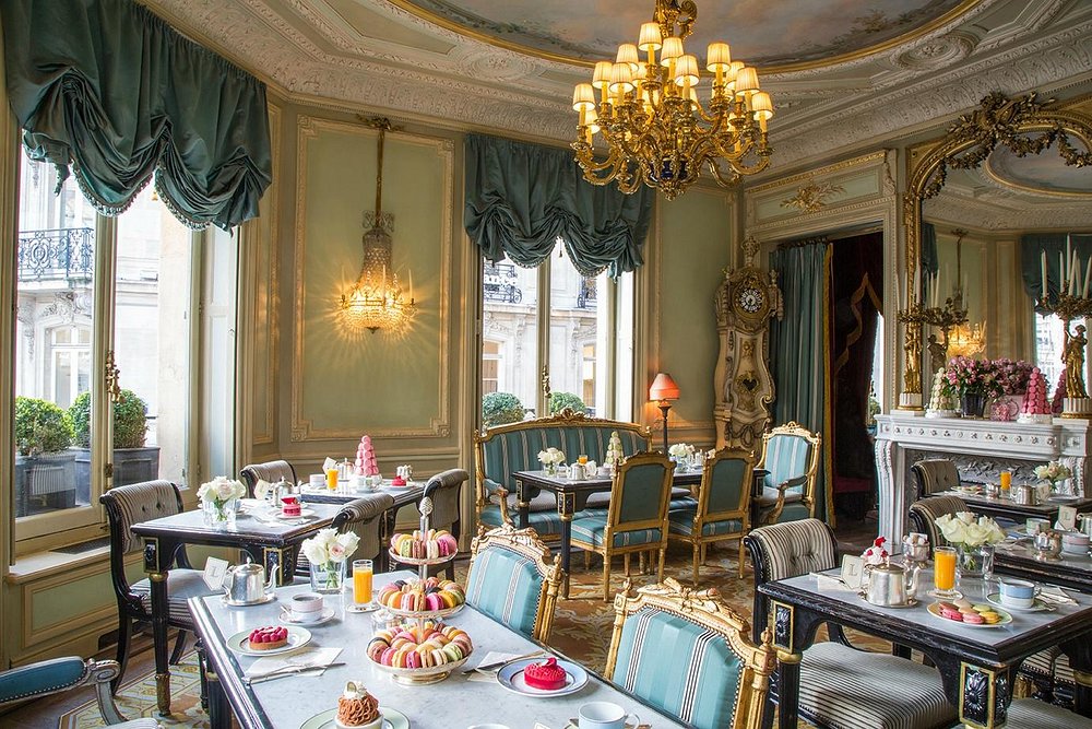 Elegant Ladurée, Paris tea room with ornate decor, a grand chandelier, and luxurious drapes. Tables set with colorful pastries, creating a sophisticated ambiance.