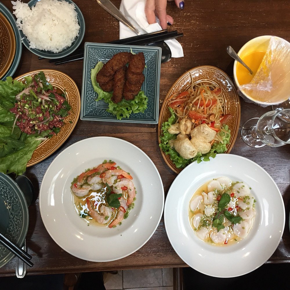 Lao Siam table with Thai dishes including raw shrimp in a spicy sauce, larb salad, and fried meat on lettuce.
