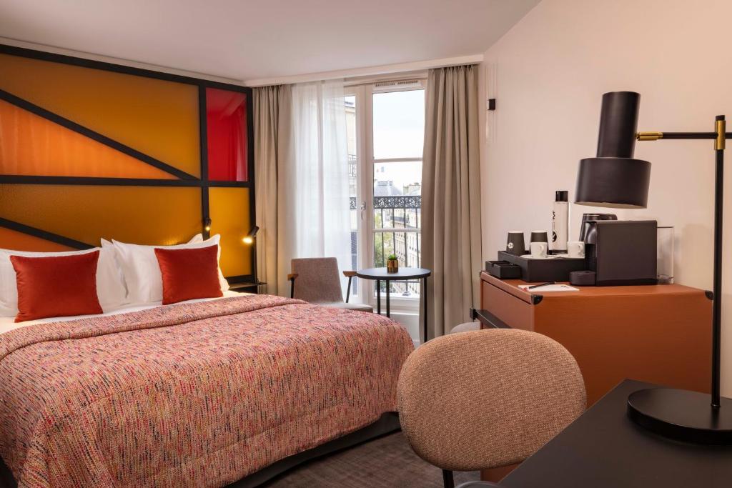 Le 12 Hôtel room with a colorful, geometric headboard, cozy bed with red pillows, balcony view, small table, and a coffee station on the desk.