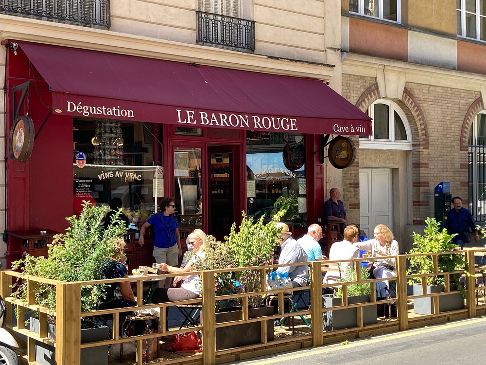 Patrons enjoying meals at outdoor tables outside Le Baron Rouge in Paris, France, with a lively street scene.
