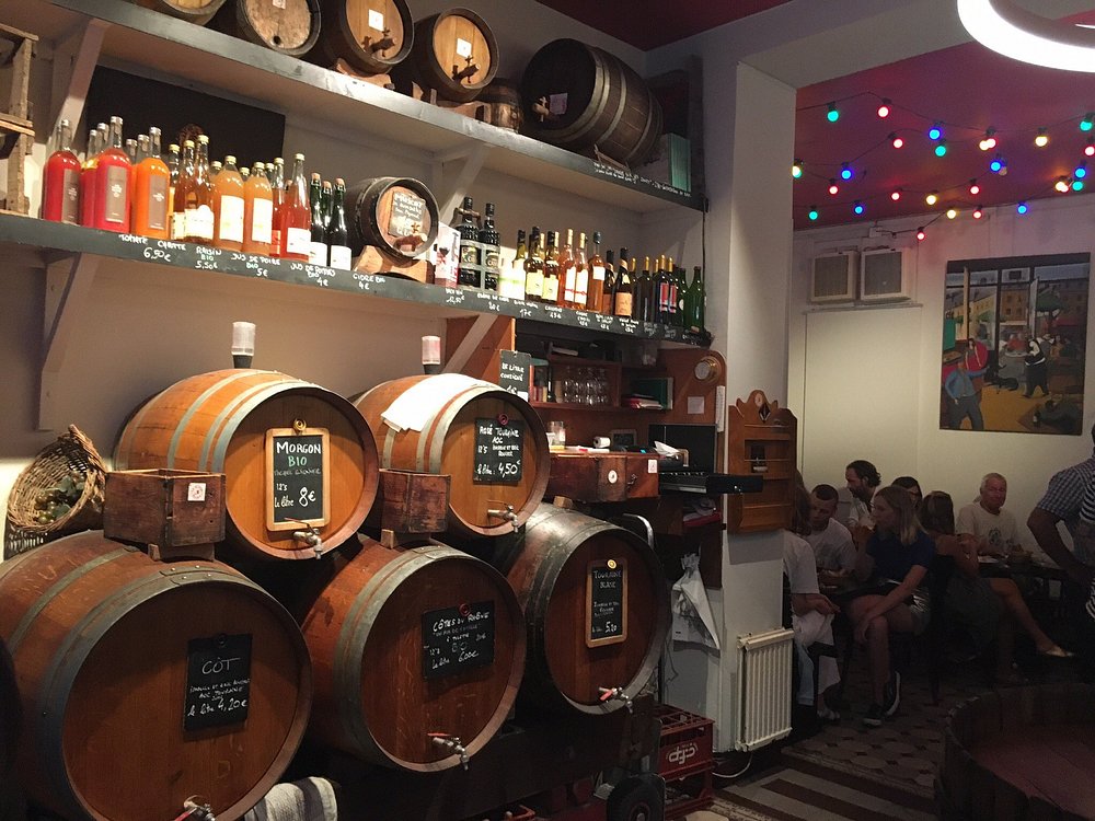 Interior of Le Baron Rouge in Paris, showcasing wine barrels and an array of bottles on display at the bar.