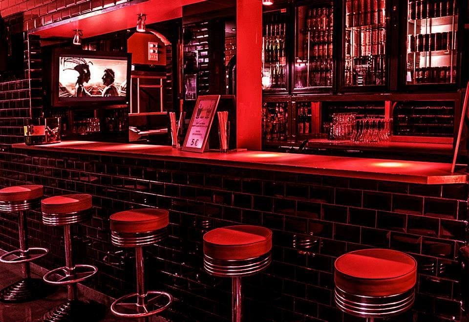 Interior of Le Depot Paris featuring a red bar, red stools, and a television.