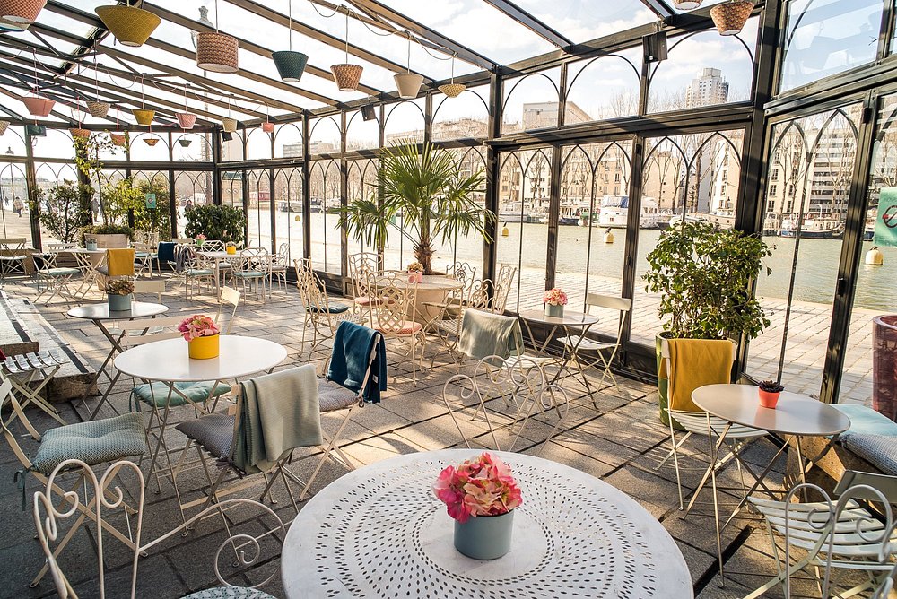 Interior of Le Pavillon des Canaux in Paris, showcasing tables and chairs beneath a transparent glass ceiling.