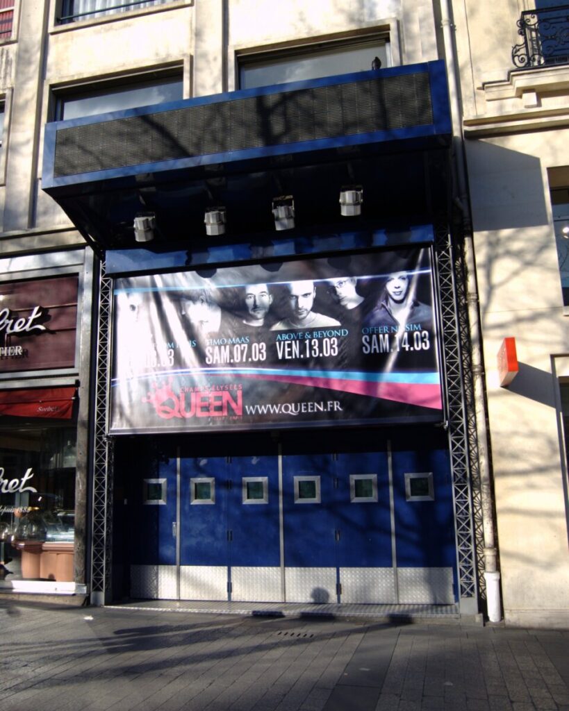 The exterior of Le Queen Paris, a prominent large blue building, stands out against the city skyline.