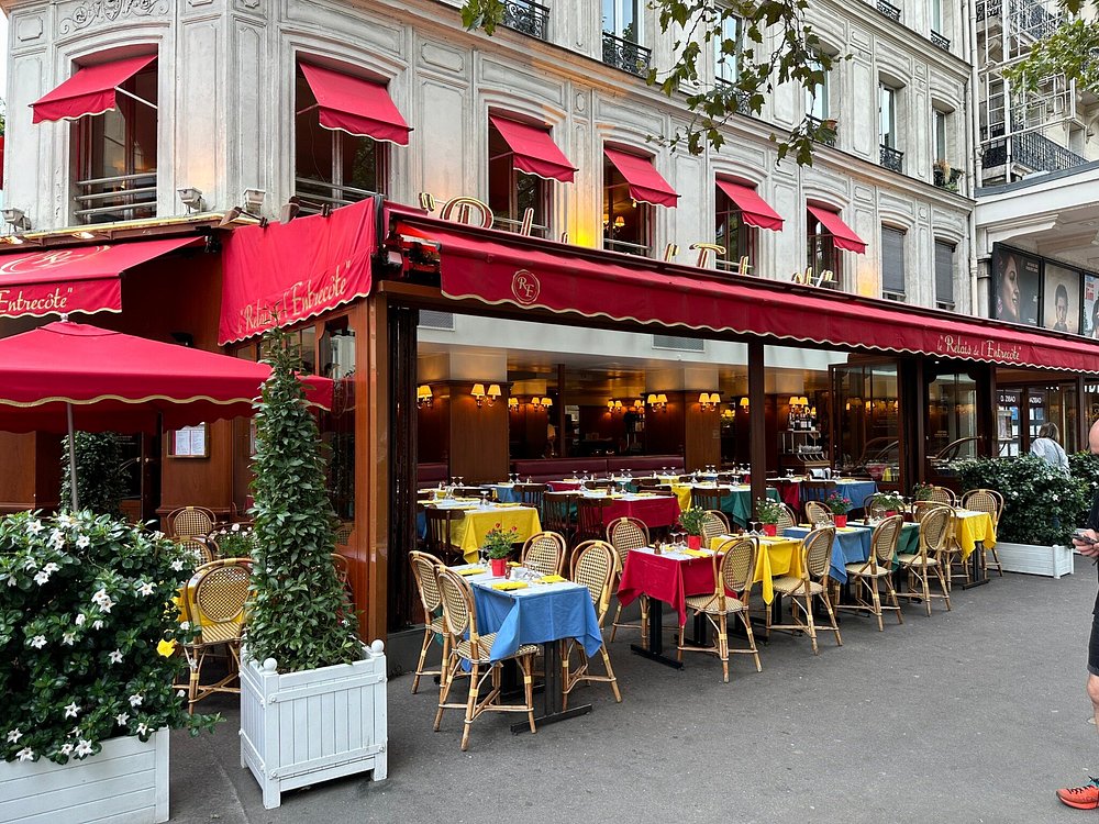 Man strolls by the Parisian restaurant Le Relais de l’Entrecôte, characterized by its vibrant red awnings.