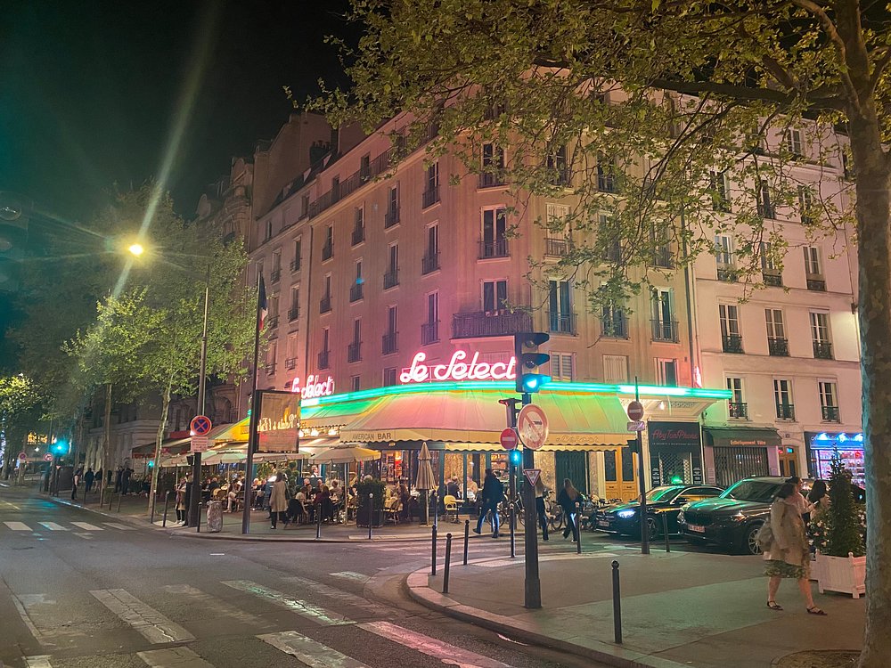 Parisian street at night, illuminated by a bright neon sign for Le Select in Montparnasse.
