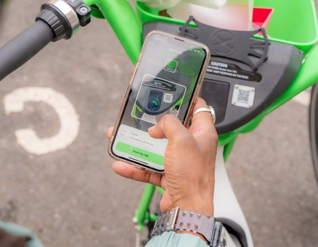 Person rides a green bicycle while using the Lime Mobile App on their smartphone.