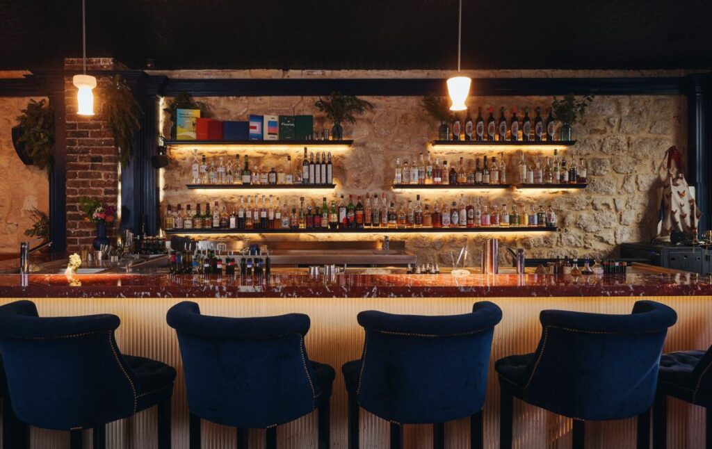 Interior of Little Red Door in Paris featuring a bar with blue chairs and a sleek counter.