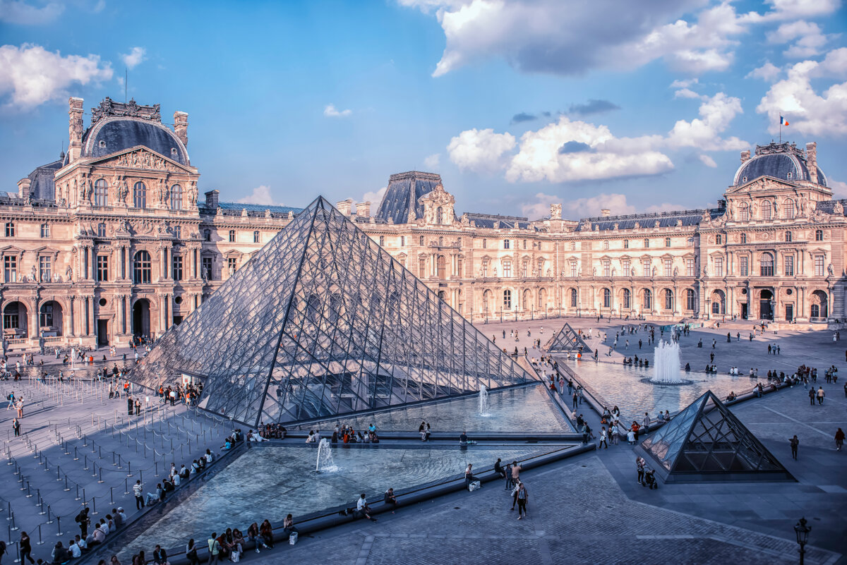 The Louvre Museum in Paris, France, showcasing its iconic glass pyramid under a clear blue sky during the daytime.