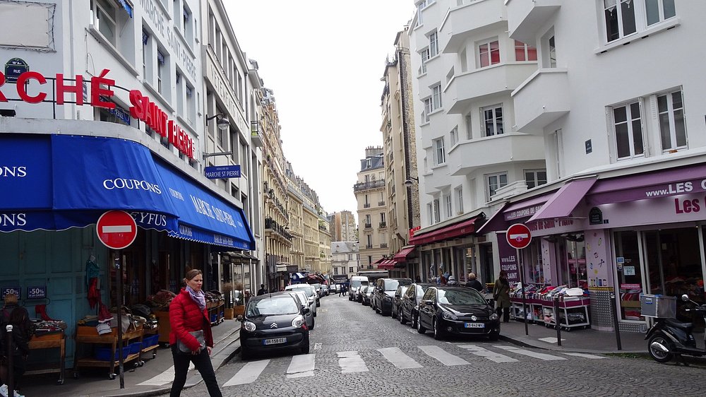 Woman strolls along a street in Paris, passing by Marché Saint-Pierre, showcasing the city's vibrant atmosphere.