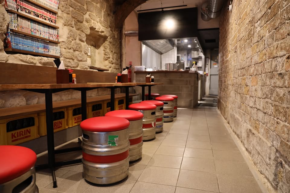 Interior of Menkicchi Ramen shop in Paris, featuring wooden decor, tables, and a vibrant atmosphere for dining