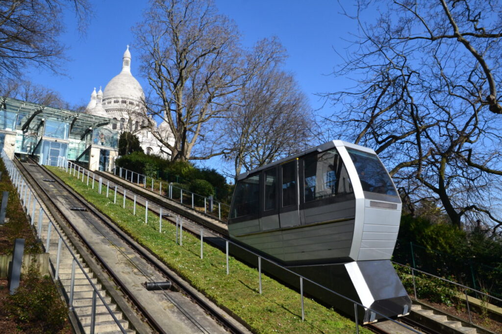 Montmartre Funicular ascending a grassy slope towards the Sacré-Cœur Basilica under a clear blue sky