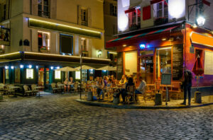 Nighttime in Montmartre, Paris, showcasing a charming street with establishment tables and easels of local artists.
