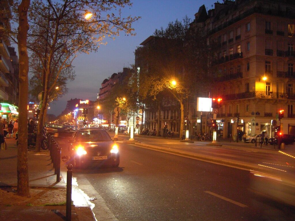 Dusk view of Montparnasse, Paris, featuring cars on a street lined with buildings illuminated by evening lights.