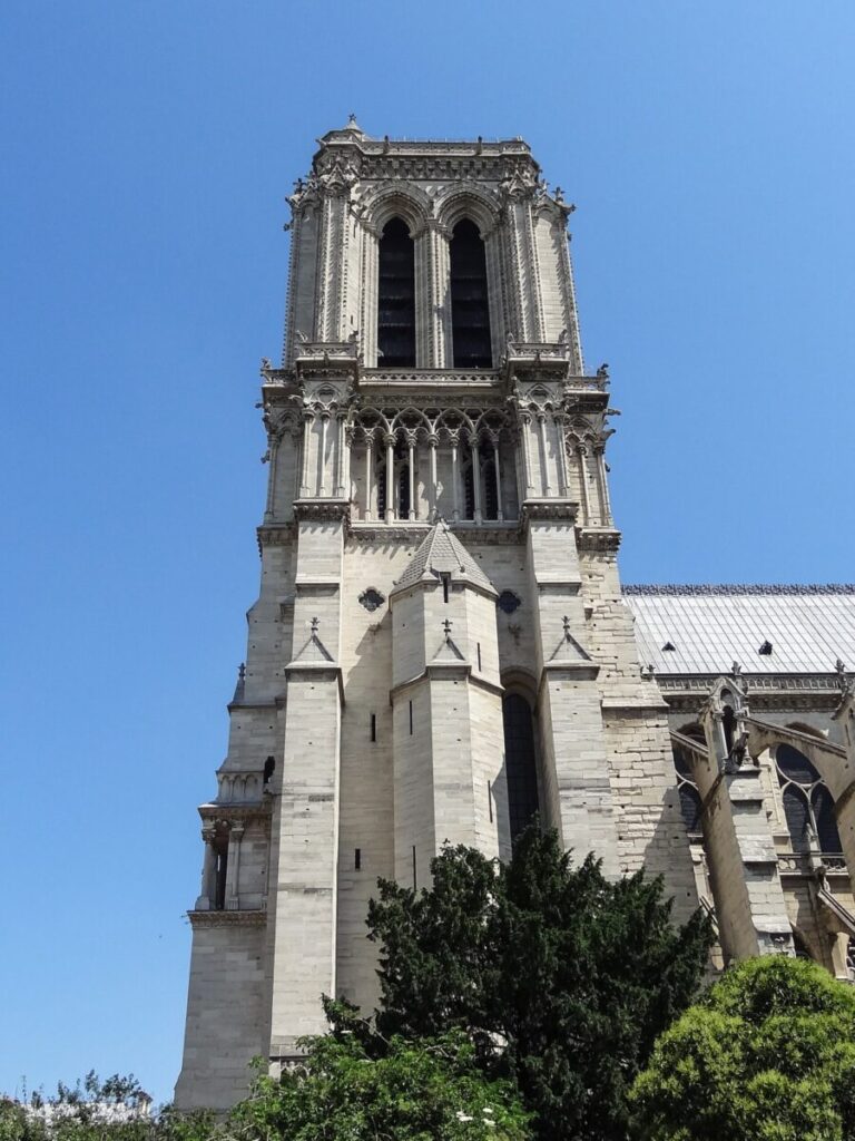The south tower of Notre Dame de Paris, featuring the iconic Emmanuel bell, stands tall against a clear blue sky.