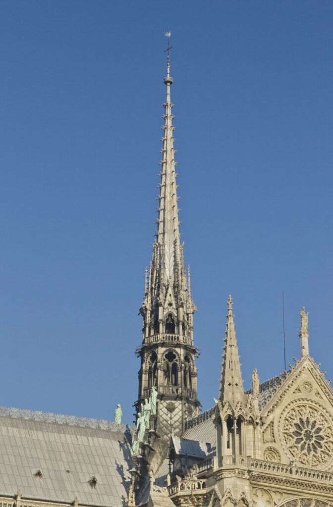 Notre-Dame de Paris spire with ornate details and a cross at the top, set against a clear blue sky, evoking a sense of history and grandeur.
