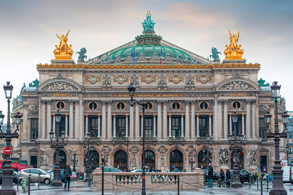 Facade of Palais Garnier in Paris on a rainy spring day, showcasing its ornate architecture and wet pavement reflections.