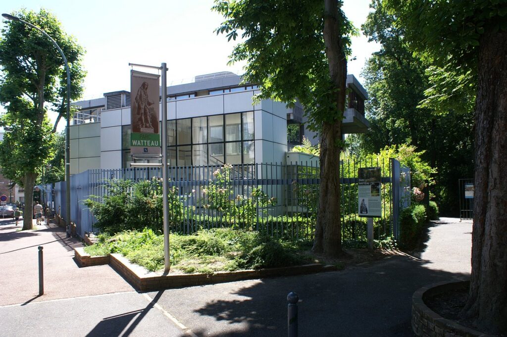 View of the area surrounding Parc Watteau, featuring adjacent residential buildings, small shops, and bustling streets with pedestrians and cyclists.