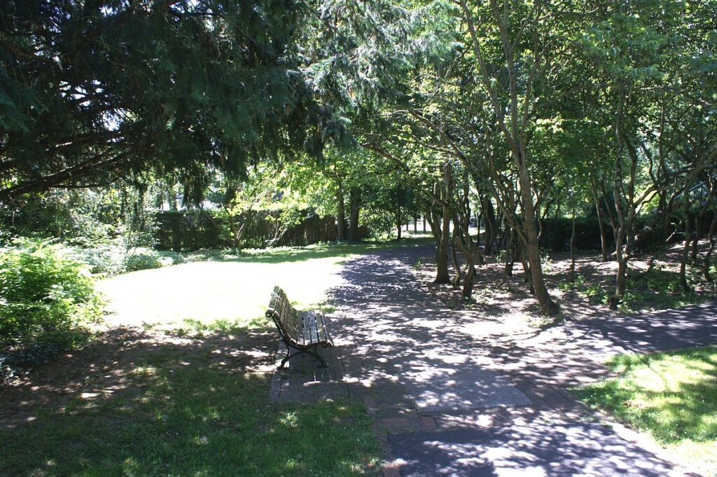 Information sign at the entrance of Parc Watteau displaying park rules, a map, and details about park amenities, with people reading the sign in the background.