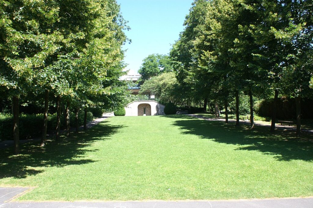 Close-up of distinct features in Parc Watteau, including a classic-style gazebo, decorative benches, and a small, ornate fountain surrounded by floral arrangements.
