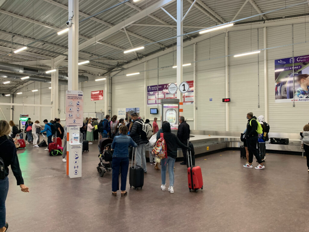 Passengers waiting in line at Paris Beauvais Airport terminal, preparing for check-in or security screening.