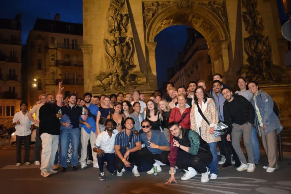 Friends gather for a photo in front of an arch, celebrating their Paris City Center guided pub crawl experience.