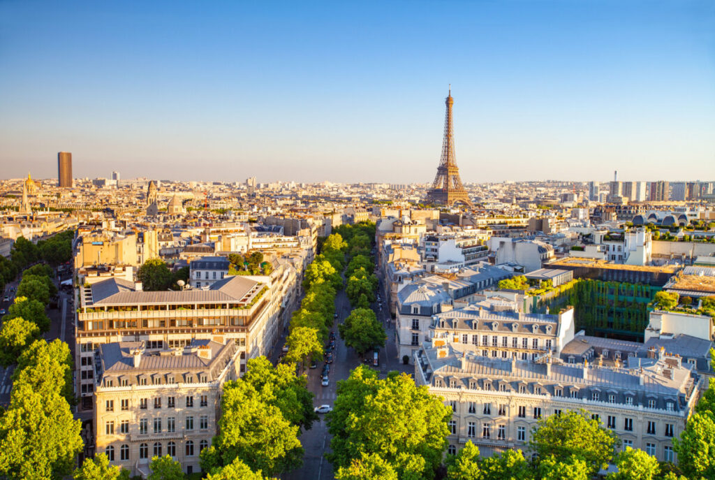 Panoramic view of Paris at sunset, showcasing the skyline with iconic landmarks silhouetted against a colorful sky.