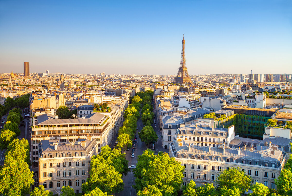 Panoramic view of Paris at sunset, showcasing the skyline with iconic landmarks silhouetted against a colorful sky.