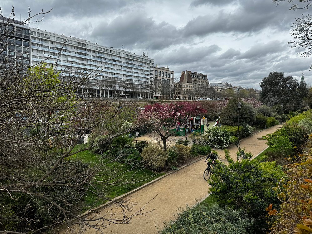 Scenic pathway with lush green bushes and a white building, set in the Paris Coulée Verte René-Dumont Garden.