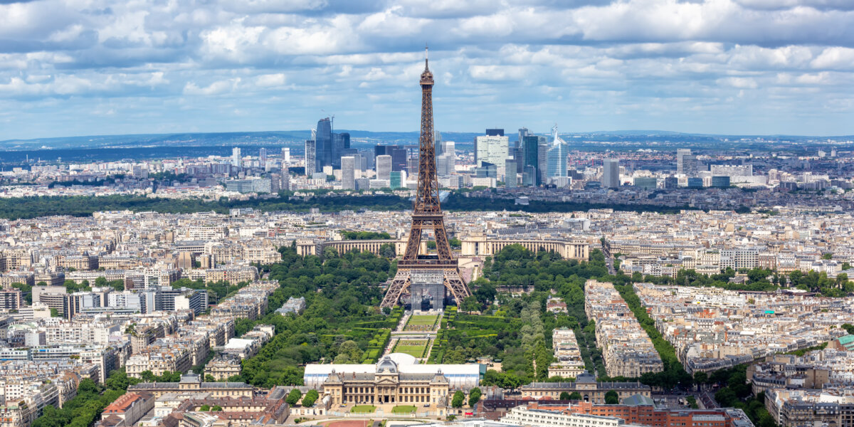 Eiffel Tower overlooking Paris with Champ de Mars and La Défense skyline under cloudy skies