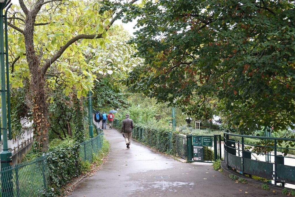 Individual strolling down a tree-lined path next to a fence in the Coulée Verte René-Dumont, Paris, France.