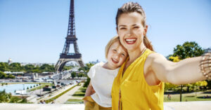 Mother and child tourists smiling while taking a selfie in front of the Eiffel Tower.