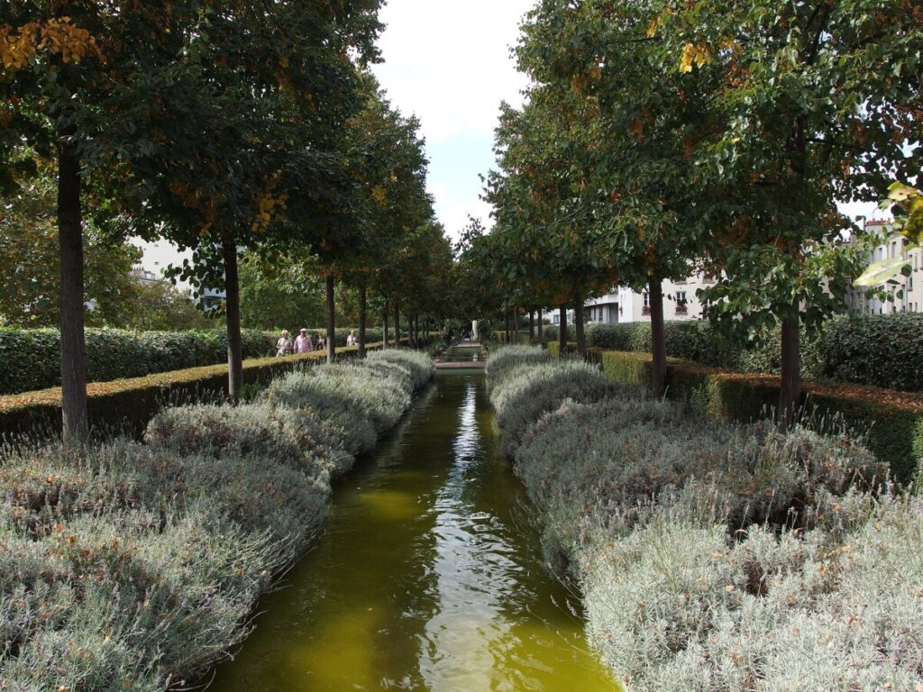 Serene canal in Paris Promenade Plantée, bordered by lush trees and vibrant bushes.
