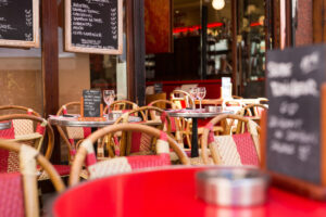 Cozy Restaurant outdoor chairs, round tables, and small menu boards. Inside, warm lighting and wine glasses add a welcoming vibe in Paris, France.