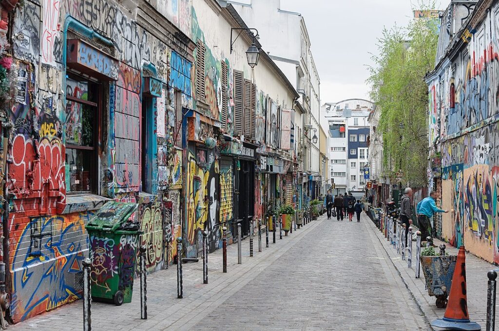 Rue Dénoyez in Paris, showcasing a narrow alley with colorful graffiti and pedestrians strolling along the lively street