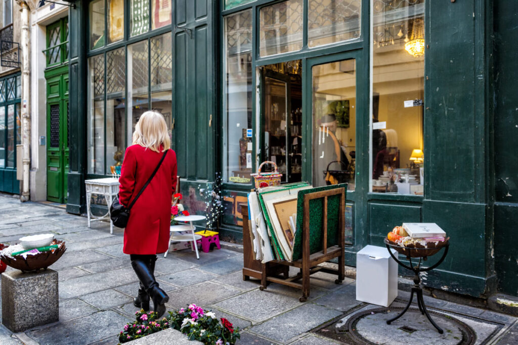 Woman walks past an antique shop with large green windows