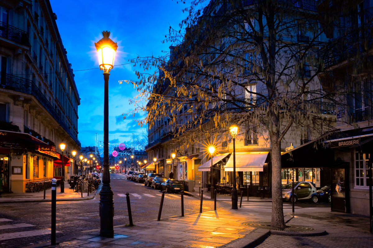 Evening view of a charming Paris street illuminated by lampposts, creating a warm and inviting atmosphere.