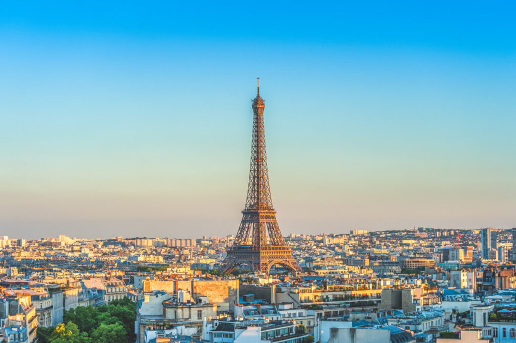 The Eiffel Tower stands tall amidst Parisian rooftops under a clear blue sky, evoking a serene and picturesque cityscape at dusk.