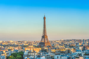 The Eiffel Tower stands tall amidst Parisian rooftops under a clear blue sky, evoking a serene and picturesque cityscape at dusk.