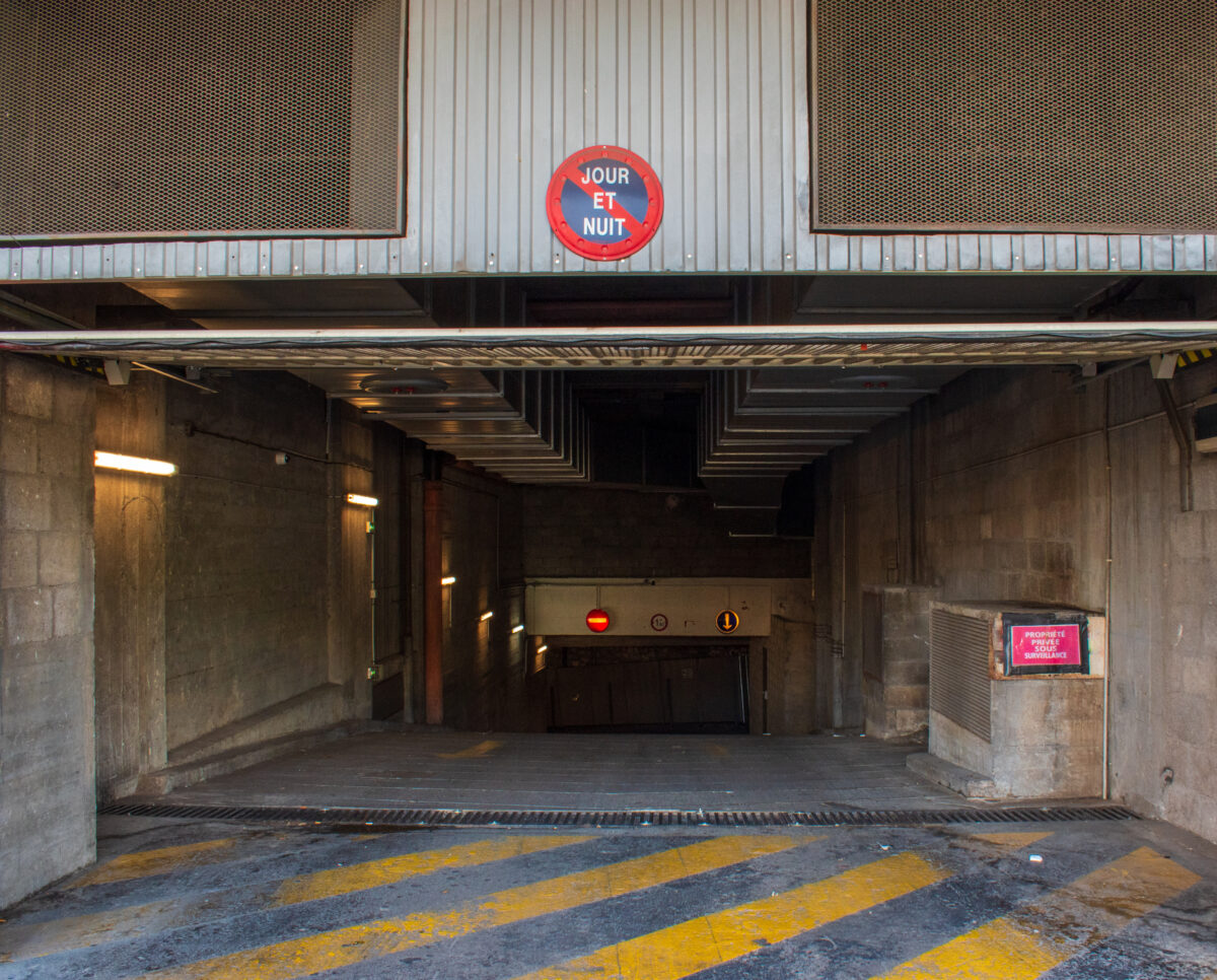 Entrance to a dimly lit, concrete underground parking garage ramp in Paris, France